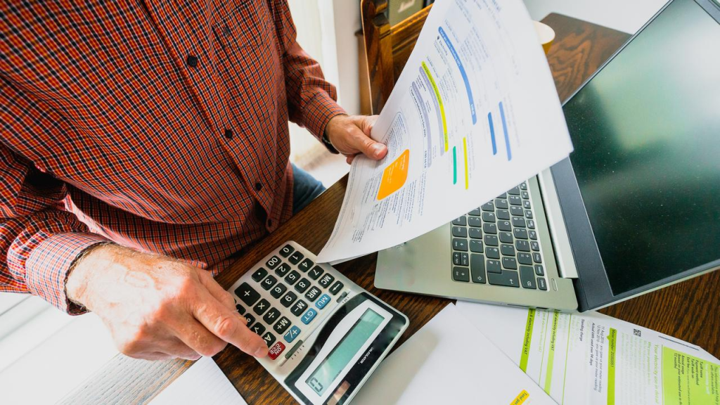 Person calculating bills with a calculator and laptop