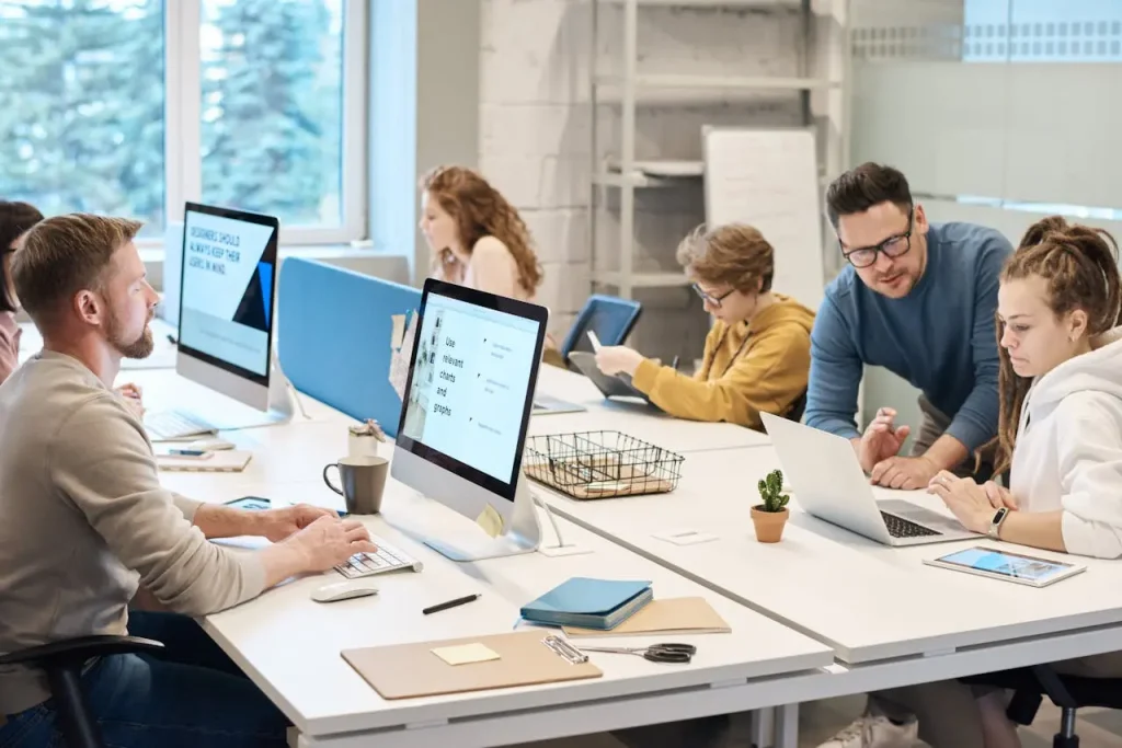Creative team collaborating in modern open-plan office with laptops and desktops
